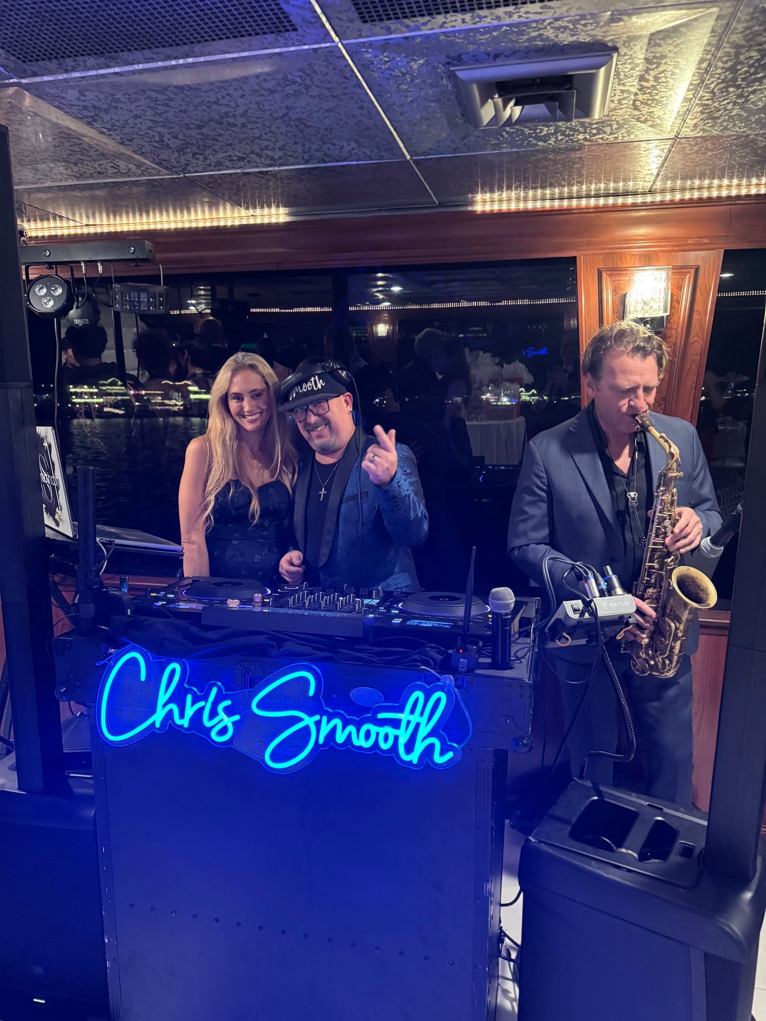 Chris Smooth at his DJ booth, the Chris Smooth neon sign lit in blue across its front